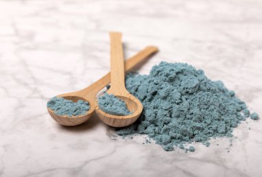 Blue spirulina powder in bowls and spoons on a marble table. Natural vegan superfood. Healthy food supplement. Phycocyanin extract. Place for text. Place for a copy.