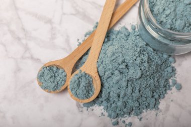 Blue spirulina powder in bowls and spoons on a marble table. Natural vegan superfood. Healthy food supplement. Phycocyanin extract. Place for text. Place for a copy.