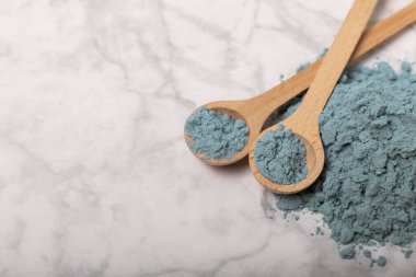 Blue spirulina powder in bowls and spoons on a marble table. Natural vegan superfood. Healthy food supplement. Phycocyanin extract. Place for text. Place for a copy.