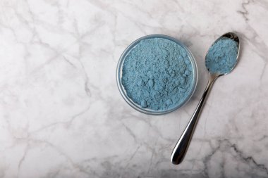 Blue spirulina powder in bowls and spoons on a marble table. Natural vegan superfood. Healthy food supplement. Phycocyanin extract. Place for text. Place for a copy.