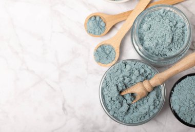 Blue spirulina powder in bowls and spoons on a marble table. Natural vegan superfood. Healthy food supplement. Phycocyanin extract. Place for text. Place for a copy.