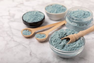 Blue spirulina powder in bowls and spoons on a marble table. Natural vegan superfood. Healthy food supplement. Phycocyanin extract. Place for text. Place for a copy.