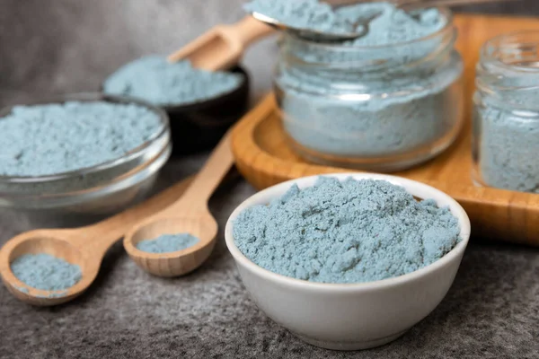 Blue spirulina powder in a bowl, jars and spoons on a black textured surface. Natural vegan superfood. Healthy food supplement. Phycocyanin extract. Place for text. Place for a copy.