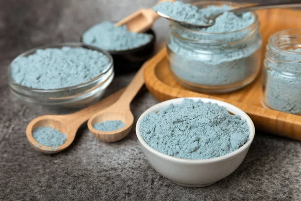 Blue spirulina powder in a bowl, jars and spoons on a black textured surface. Natural vegan superfood. Healthy food supplement. Phycocyanin extract. Place for text. Place for a copy.