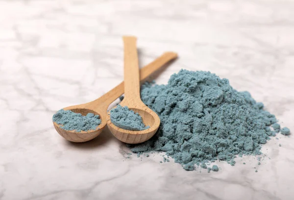 Blue spirulina powder in bowls and spoons on a marble table. Natural vegan superfood. Healthy food supplement. Phycocyanin extract. Place for text. Place for a copy.
