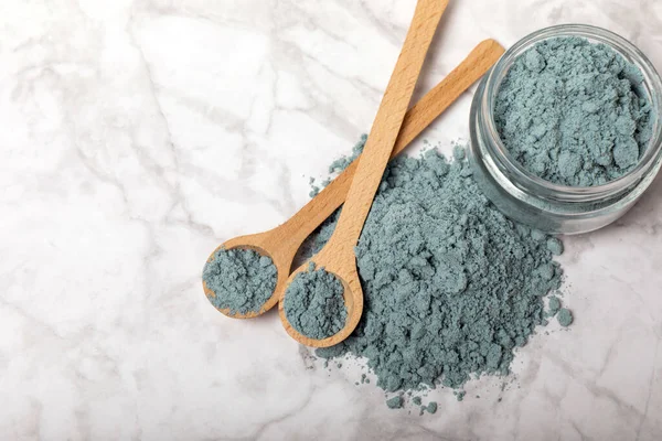 Blue spirulina powder in bowls and spoons on a marble table. Natural vegan superfood. Healthy food supplement. Phycocyanin extract. Place for text. Place for a copy.