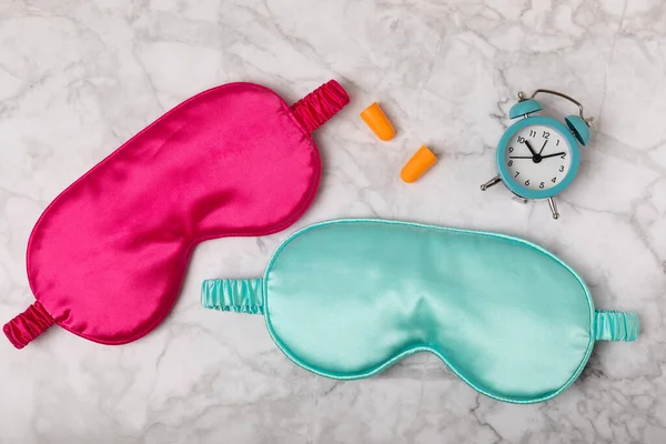 Sleep mask on a marble background. Sleep mask, alarm clock, insomnia pills and earplugs. The concept of rest, sleep quality, good night, insomnia and relaxation. View from above. Place for text. MOCAP