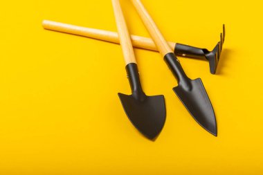 Sarı arka planda bahçe aletleri, üst manzara. Bahçe kürekleri ve tırmıklar. Bahçe işleri, peyzaj ve hobi anlayışı. Metin için yer.