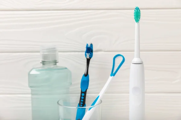Electronic ultrasonic toothbrush, mouthwash, floss, tongue cleaner and toothpaste on white wooden background. Items for dental care and caries prevention in the bathroom. Dentistry concept. Copy space.