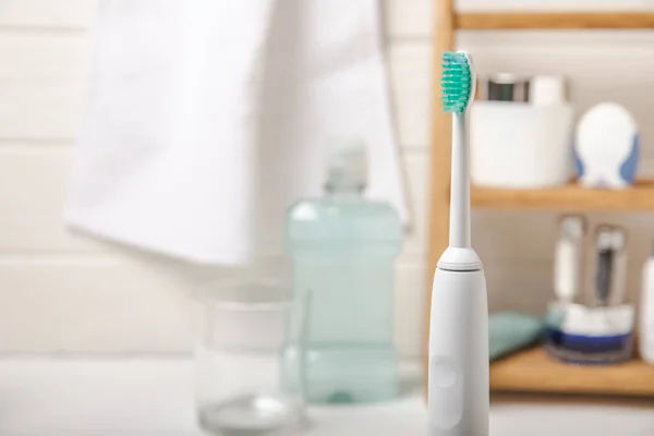 Electronic ultrasonic toothbrush, mouthwash, floss, tongue cleaner and toothpaste on white wooden background. Items for dental care and caries prevention in the bathroom. Dentistry concept. Copy space.