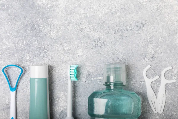 Electronic ultrasonic toothbrush, mouthwash, floss, tongue cleaner and toothpaste on blue textured background. Items for dental care and caries prevention in the bathroom. Dentistry concept. Copy space.