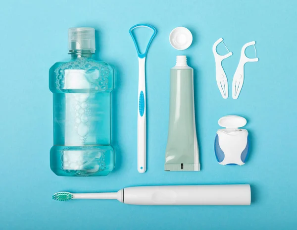 Electronic ultrasonic toothbrush, mouthwash, floss, tongue cleaner and toothpaste on blue textured background. Items for dental care and caries prevention in the bathroom. Dentistry concept. Copy space.