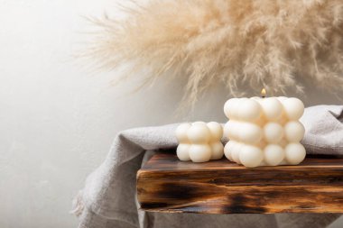 Beyaz desenli bir masada soya mumu. Yanan bir baloncuk mumunun iç dekorasyonu. Hygge ev dekorasyonu konsepti ve aromaterapi. Konforlu ev tasarımı. Mesaj için yer. Kopyalanacak yer.