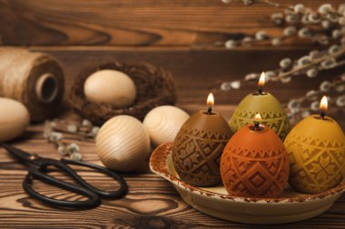 Kahverengi desenli bir tabakta paskalya mumu yumurtaları. Paskalya bayramı konsepti. Söğüt buketi. Ev dekorasyonu ve festival çeliği. Metin için yer.