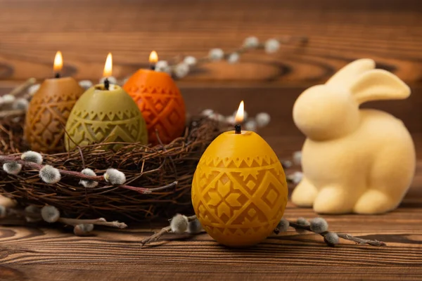 Easter candle eggs in a nest with an easter bunny on a brown textural background. Easter holiday concept.Spring willow bouquet.Decor for home and festive steel.Copy space. Place for text.