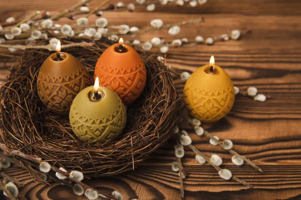 Easter candle eggs in a nest with an easter bunny on a brown textural background. Easter holiday concept.Spring willow bouquet.Decor for home and festive steel.Copy space. Place for text.
