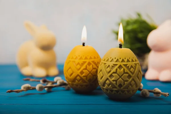 Easter candle eggs, Easter bunny and willow branches on a blue table and a blurred light background. Easter holiday concept.Spring willow bouquet.Decor for home and festive steel.Copy space. Place for text.