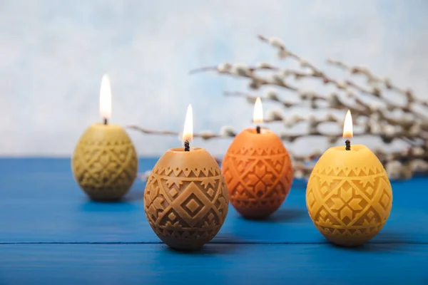 Easter candle eggs and willow branches on a blue table and a blurred light background. Easter holiday concept.Spring willow bouquet.Decor for home and festive steel.Copy space. Place for text.