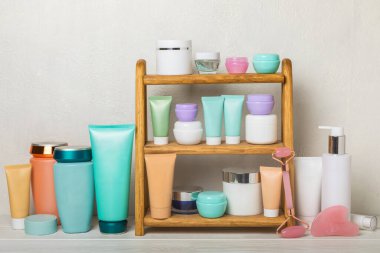 Banyoda beyaz bir duvara yaslanmış kozmetik ürünleri olan raflar. Yıkama jölesi, toner, serum ve vücut kremi, gua sha masaj silindiri, şampuan ve saç kremi. Dekoratif ve bakım kozmetiği. Güzellik konsepti..