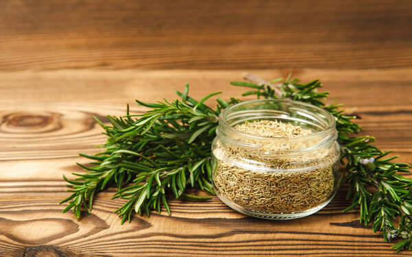Сушеный розмарин в стеклянной банке, ветви свежего розмарина на коричневом деревянном фоне. Специи и травы для мяса и fish.Recipe.Culinary concept.Organic трав. Место для текста.
