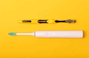 Sarı arka planda elektrikli ve manuel diş fırçaları. Yukarıdan bak. Ağız temizliği. Sıradan diş fırçası, eko ve elektrikli diş fırçası. Ağız temizliği. Ağız bakım kiti. Dişçi konsepti. Diş bakımı.