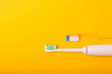 Sarı arka planda elektrikli ve manuel diş fırçaları. Yukarıdan bak. Ağız temizliği. Sıradan diş fırçası, eko ve elektrikli diş fırçası. Ağız temizliği. Ağız bakım kiti. Dişçi konsepti. Diş bakımı.