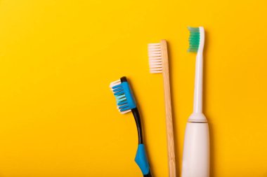 Sarı arka planda elektrikli ve manuel diş fırçaları. Yukarıdan bak. Ağız temizliği. Sıradan diş fırçası, eko ve elektrikli diş fırçası. Ağız temizliği. Ağız bakım kiti. Dişçi konsepti. Diş bakımı.
