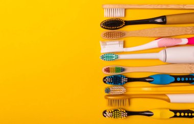 Sarı arka planda elektrikli ve manuel diş fırçaları. Yukarıdan bak. Ağız temizliği. Sıradan diş fırçası, eko ve elektrikli diş fırçası. Ağız temizliği. Ağız bakım kiti. Dişçi konsepti. Diş bakımı.