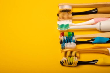 Sarı arka planda elektrikli ve manuel diş fırçaları. Yukarıdan bak. Ağız temizliği. Sıradan diş fırçası, eko ve elektrikli diş fırçası. Ağız temizliği. Ağız bakım kiti. Dişçi konsepti. Diş bakımı.