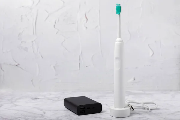 A modern electric toothbrush is charged from an external power bank battery on a marble background. Smart electric toothbrush on a pink background.Modern technologies for health. Healthy teeth. Dentistry concept.