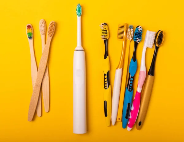 Electric and manual toothbrushes on a yellow background. View from above. Oral hygiene. Ordinary toothbrush, eco and electric toothbrush. Oral hygiene. Oral Care Kit. Dentist concept. Dental care.
