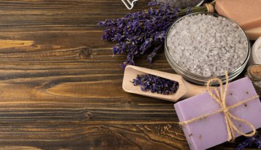 Lavanta kaplıcası. Temel yağlar, deniz tuzu, el yapımı sabun, krem ve vücut fırçası kahverengi desenli ahşap lavanta çiçekleri. Çiçekli doğal bitkisel kozmetik ürünleri ve lavanta aroması..