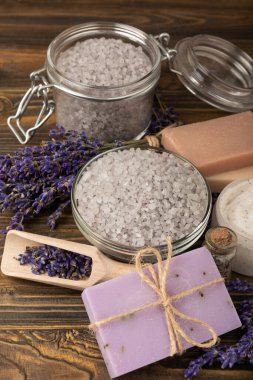Lavanta kaplıcası. Temel yağlar, deniz tuzu, el yapımı sabun, krem ve vücut fırçası kahverengi desenli ahşap lavanta çiçekleri. Çiçekli doğal bitkisel kozmetik ürünleri ve lavanta aroması..