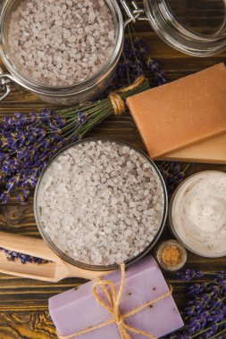 Lavanta kaplıcası. Temel yağlar, deniz tuzu, el yapımı sabun, krem ve vücut fırçası kahverengi desenli ahşap lavanta çiçekleri. Çiçekli doğal bitkisel kozmetik ürünleri ve lavanta aroması..