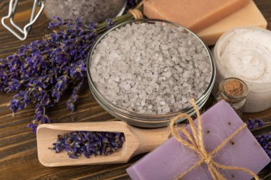 Lavanta kaplıcası. Temel yağlar, deniz tuzu, el yapımı sabun, krem ve vücut fırçası kahverengi desenli ahşap lavanta çiçekleri. Çiçekli doğal bitkisel kozmetik ürünleri ve lavanta aroması..