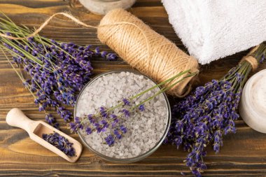 Lavanta kaplıcası. Temel yağlar, deniz tuzu, el yapımı sabun, krem ve vücut fırçası kahverengi desenli ahşap lavanta çiçekleri. Çiçekli doğal bitkisel kozmetik ürünleri ve lavanta aroması..