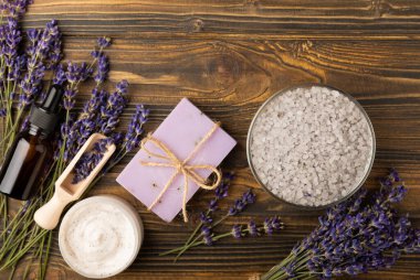 Lavanta kaplıcası. Temel yağlar, deniz tuzu, el yapımı sabun, krem ve vücut fırçası kahverengi desenli ahşap lavanta çiçekleri. Çiçekli doğal bitkisel kozmetik ürünleri ve lavanta aroması..