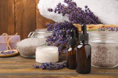 Lavanta kaplıcası. Temel yağlar, deniz tuzu, el yapımı sabun, krem ve vücut fırçası kahverengi desenli ahşap lavanta çiçekleri. Çiçekli doğal bitkisel kozmetik ürünleri ve lavanta aroması..