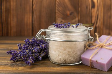 Lavanta kaplıcası. Temel yağlar, deniz tuzu, el yapımı sabun, krem ve vücut fırçası kahverengi desenli ahşap lavanta çiçekleri. Çiçekli doğal bitkisel kozmetik ürünleri ve lavanta aroması..
