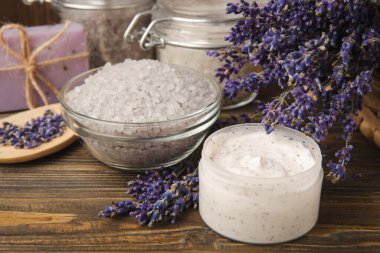 Lavanta kaplıcası. Temel yağlar, deniz tuzu, el yapımı sabun, krem ve vücut fırçası kahverengi desenli ahşap lavanta çiçekleri. Çiçekli doğal bitkisel kozmetik ürünleri ve lavanta aroması..