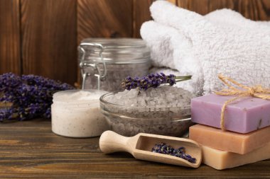 Lavanta kaplıcası. Temel yağlar, deniz tuzu, el yapımı sabun, krem ve vücut fırçası kahverengi desenli ahşap lavanta çiçekleri. Çiçekli doğal bitkisel kozmetik ürünleri ve lavanta aroması..
