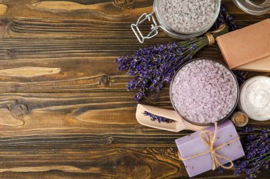 Lavanta kaplıcası. Temel yağlar, deniz tuzu, el yapımı sabun, krem ve vücut fırçası kahverengi desenli ahşap lavanta çiçekleri. Çiçekli doğal bitkisel kozmetik ürünleri ve lavanta aroması..