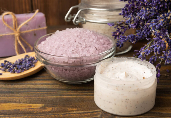 Лавандовый курорт. Эфирные масла, морская соль, мыло ручной работы, крем и скраб для тела с цветами лаванды на коричневой текстуре дерева. Натуральная травяная косметика с цветами и ароматом лаванды. Ароматерапия и отдых.