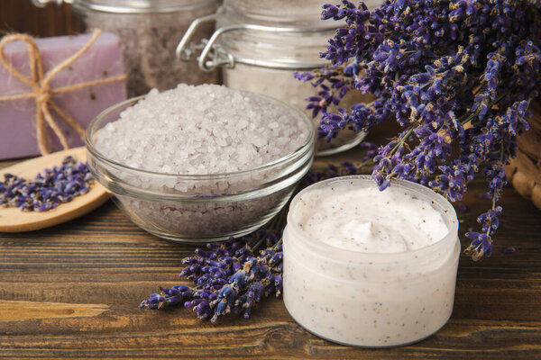 Лавандовый курорт. Эфирные масла, морская соль, мыло ручной работы, крем и скраб для тела с цветами лаванды на коричневой текстуре дерева. Натуральная травяная косметика с цветами и ароматом лаванды. Ароматерапия и отдых.