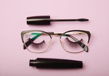 Takma kirpikli, gözlüklü, rimel ve kirpik fırçalı, pembe arka planda kirpik bigudileri. Makyaj aletleri. Güzellik konsepti. Beste yap. Mesaj için yer. Kopyalanacak yer. Düz. 