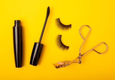 Takma kirpikler, rimel ve kirpik fırçaları, sarı arka planda kirpik bigudileri. Makyaj aletleri. Güzellik konsepti. Beste yap. Mesaj için yer. Kopyalanacak yer. Düz çizgi. MOCAP.