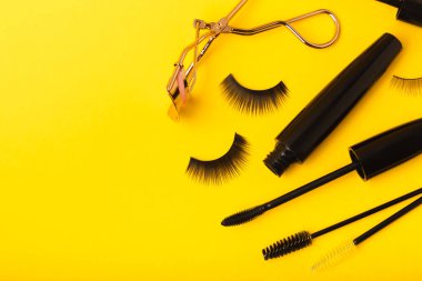 Takma kirpikler, rimel ve kirpik fırçaları, sarı arka planda kirpik bigudileri. Makyaj aletleri. Güzellik konsepti. Beste yap. Mesaj için yer. Kopyalanacak yer. Düz çizgi. MOCAP.
