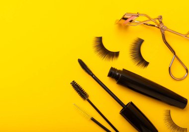 Takma kirpikler, rimel ve kirpik fırçaları, sarı arka planda kirpik bigudileri. Makyaj aletleri. Güzellik konsepti. Beste yap. Mesaj için yer. Kopyalanacak yer. Düz çizgi. MOCAP.