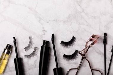 Takma kirpikli, rimel ve kirpik fırçalı, mermer arka planda kirpik bigudileri. Makyaj aletleri. Güzellik konsepti. Beste yap. Mesaj için yer. Kopyalanacak yer. Düz çizgi. MOCAP.