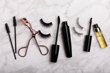 Takma kirpikli, rimel ve kirpik fırçalı, mermer arka planda kirpik bigudileri. Makyaj aletleri. Güzellik konsepti. Beste yap. Mesaj için yer. Kopyalanacak yer. Düz çizgi. MOCAP.